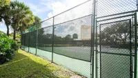 Inviting tennis court surrounded by lush greenery and palm trees under a bright blue sky.