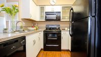 Inviting kitchen with sleek black appliances, modern countertops, and elegant cabinetry, accented by vibrant sunflowers and cozy wooden flooring.