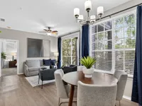 Elegant living room with modern decor, featuring a cozy gray sofa, stylish accent chairs, and a chic dining area bathed in natural light from large windows.