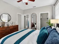Elegant bedroom with a modern design featuring a cozy bed adorned with blue pillows, a wooden dresser with decorative accents, and abundant natural light.