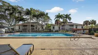 Inviting apartment complex with a sparkling pool, surrounded by lush palm trees and sun loungers, perfect for relaxation and enjoyment.