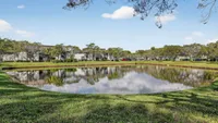 Beautiful apartment complex reflected in a serene pond surrounded by lush greenery and vibrant trees.