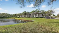 Charming apartment complex with serene lakeside views, surrounded by lush greenery and palm trees.