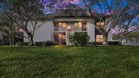 Charming apartment building surrounded by lush greenery and mature trees at dusk, offering serene living with inviting balconies and well-lit entrances.