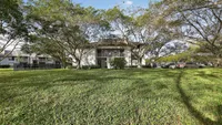 Charming apartment complex nestled among lush trees with a spacious green lawn, offering serene living and ample parking.