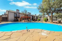 Inviting apartment complex with a sparkling blue swimming pool, surrounded by lush greenery and a charming wooden pergola, perfect for relaxation and outdoor gatherings.