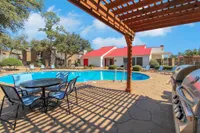 Inviting outdoor pool area with modern seating, surrounded by lush greenery and charming red-roofed clubhouse, perfect for relaxation and leisure.