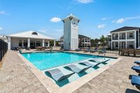 Luxurious apartment complex featuring a sparkling pool, comfortable lounge chairs, and a stylish clock tower under a clear blue sky.
