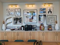 Chic apartment lobby area featuring modern art gallery wall above stylish wooden cabinets, equipped with a gourmet coffee station and array of snacks for a welcoming atmosphere.