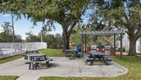 Inviting outdoor picnic area with multiple picnic tables under lush trees and a modern BBQ grill station, perfect for gatherings.