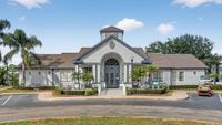 Charming clubhouse with classic architecture, surrounded by lush landscaping and palm trees, offering an inviting entrance and ample parking.