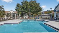 Inviting outdoor pool area with sun loungers, surrounded by lush landscaping and modern apartment buildings under a clear blue sky.