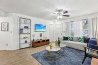 Inviting living room with modern decor, featuring a stylish sofa, elegant glass coffee tables, and a wall-mounted flat-screen TV, all bathed in natural light from large windows.