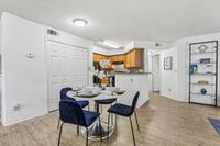 Bright dining area with elegant velvet chairs and marble table, adjacent to a stylish kitchen with modern wood cabinets and mosaic backsplash.
