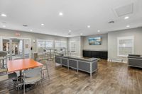Modern and inviting community room with sleek furniture, large windows, and a vibrant orange table, perfect for social gatherings.