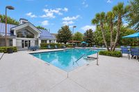 Inviting apartment pool area featuring crystal-clear water, elegant poolside seating, and lush landscaping under a bright blue sky.