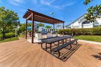 Outdoor communal area with modern grill stations and shaded seating, surrounded by lush greenery under a bright blue sky.