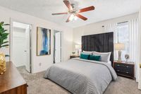 Elegant bedroom with plush carpet, stylish bedding, and chic decor, featuring a modern ceiling fan and natural light through large windows.