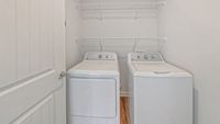 Modern laundry room featuring sleek white washer and dryer with overhead shelving for storage.