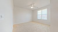 Bright, cozy room with plush carpeting and a ceiling fan, illuminated by natural light from a large window with blinds.