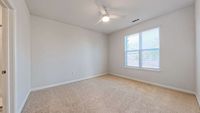 Bright and airy bedroom with plush carpet, large window offering natural light, and a modern ceiling fan.