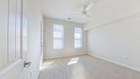 Bright, airy room with plush carpet, two large windows inviting natural light, and a ceiling fan for comfort.