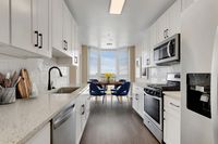 Modern kitchen with sleek white cabinets, stainless steel appliances, and a cozy dining area with blue chairs by large windows.