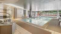 Luxurious indoor pool area with modern lounge chairs and large windows offering scenic views at upscale apartment complex.
