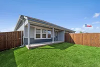 Charming backyard view of a modern house with a well-maintained lawn and a wooden fence, under a clear blue sky.