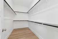 Spacious and elegant walk-in closet with sleek design and ample hanging space, featuring polished wooden flooring and bright white walls.