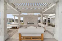 Elegant outdoor lounge area with modern white pergola, stylish seating, and a cozy fireplace beside a refreshing pool, perfect for relaxation and entertaining.