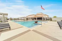 Luxurious apartment complex featuring an inviting pool area with stylish lounge chairs and pergolas, complemented by a striking American flag under a clear blue sky.