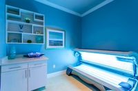 Modern tanning room with sleek sunbed and elegant blue decor, complemented by stylish shelving and artistic wall art.