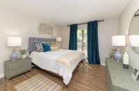 Inviting bedroom featuring plush decor with vibrant teal curtains, a luxurious bed set, and elegant lighting on wooden flooring.