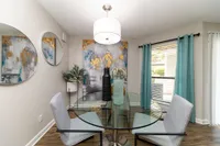 Elegant dining area with modern glass table and abstract artwork, featuring chic decor and large windows for natural light.