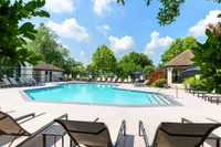 Inviting outdoor pool area with comfortable lounge chairs, surrounded by lush greenery and a clear blue sky, perfect for relaxation and leisure.