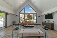 Bright and inviting living room with vaulted ceiling, stylish furniture, and large windows offering a view of the lush outdoor landscape.