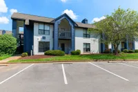 Charming two-story apartment building with modern blue and white facade, surrounded by lush landscaping and open parking spaces.