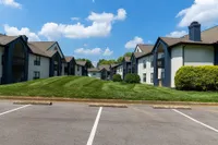 Charming apartment complex with modern architecture, lush green lawns, and bright blue skies, offering a welcoming and serene living environment.