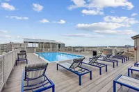 Stunning rooftop pool with modern lounge chairs offering panoramic city views under a vibrant blue sky.