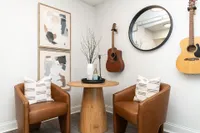Chic corner featuring modern leather chairs, a stylish round wooden table, and artistic wall decor with guitars enhancing a cozy vibe.