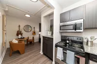 Modern apartment kitchen with stainless steel appliances, granite countertops, and cozy dining nook featuring leather chairs and decorative guitars on the wall.