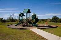 Inviting playground with vibrant green slides and climbing structures, set in a scenic park with a clear blue sky.