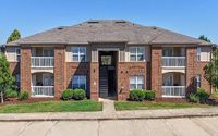 Charming two-story brick apartment building with white balconies, well-maintained landscaping, and inviting central entrance.
