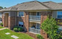 Charming two-story apartment building with brick facade, private balconies, and lush green surroundings.