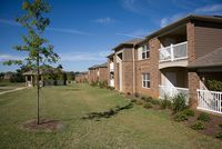 Charming apartment complex with red brick exterior and private balconies overlooking a lush green lawn and serene landscape.