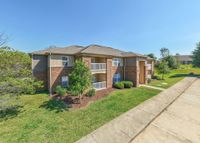 Charming two-story apartment building with brick exterior nestled in a lush green landscape, promising a serene and spacious living environment.