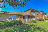 Charming two-story apartment with brick and siding exterior, featuring private balconies and lush landscaping under a clear blue sky.