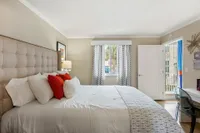 Inviting bedroom with a plush tufted headboard, vibrant cushions, and a sunlit window offering a serene view.