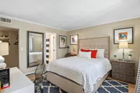 Inviting bedroom showcasing a plush bed with stylish red and white accents, elegant mirrored decor, and warm lighting.